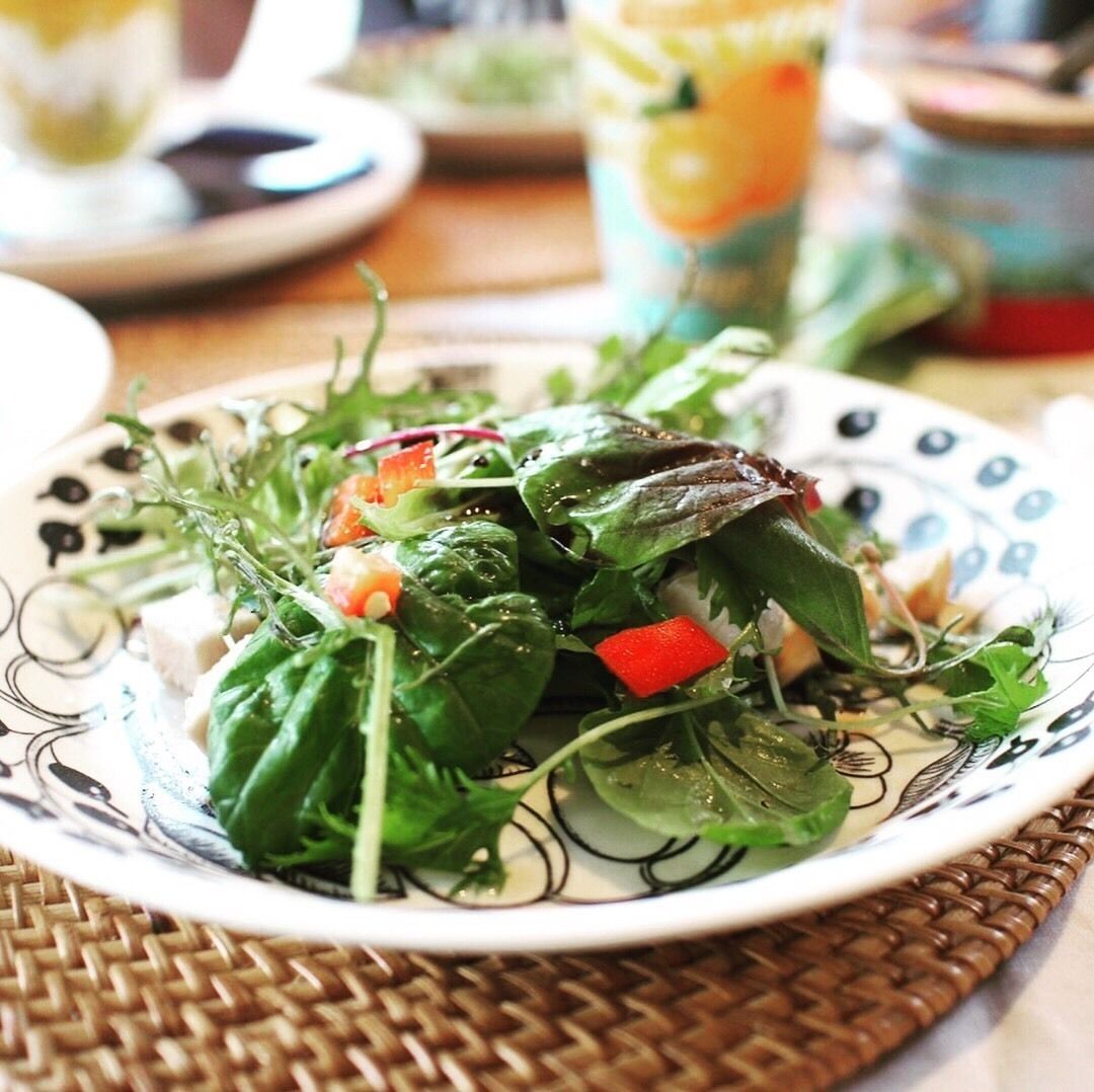 A plate of mixed greens salad with red bell peppers and cheese on a decorative plate.