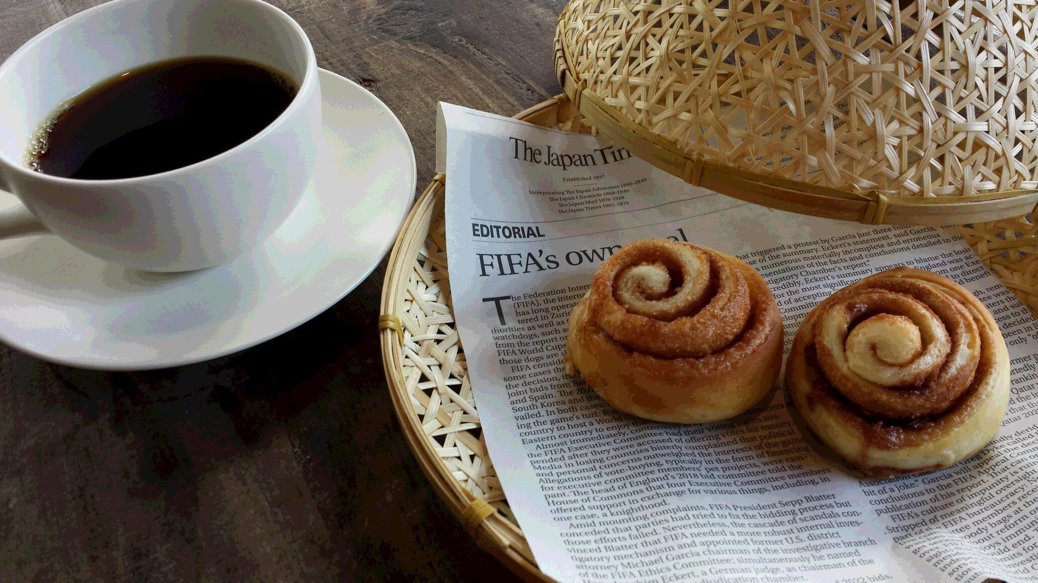 A cup of coffee, a newspaper, and two cinnamon rolls on a table.