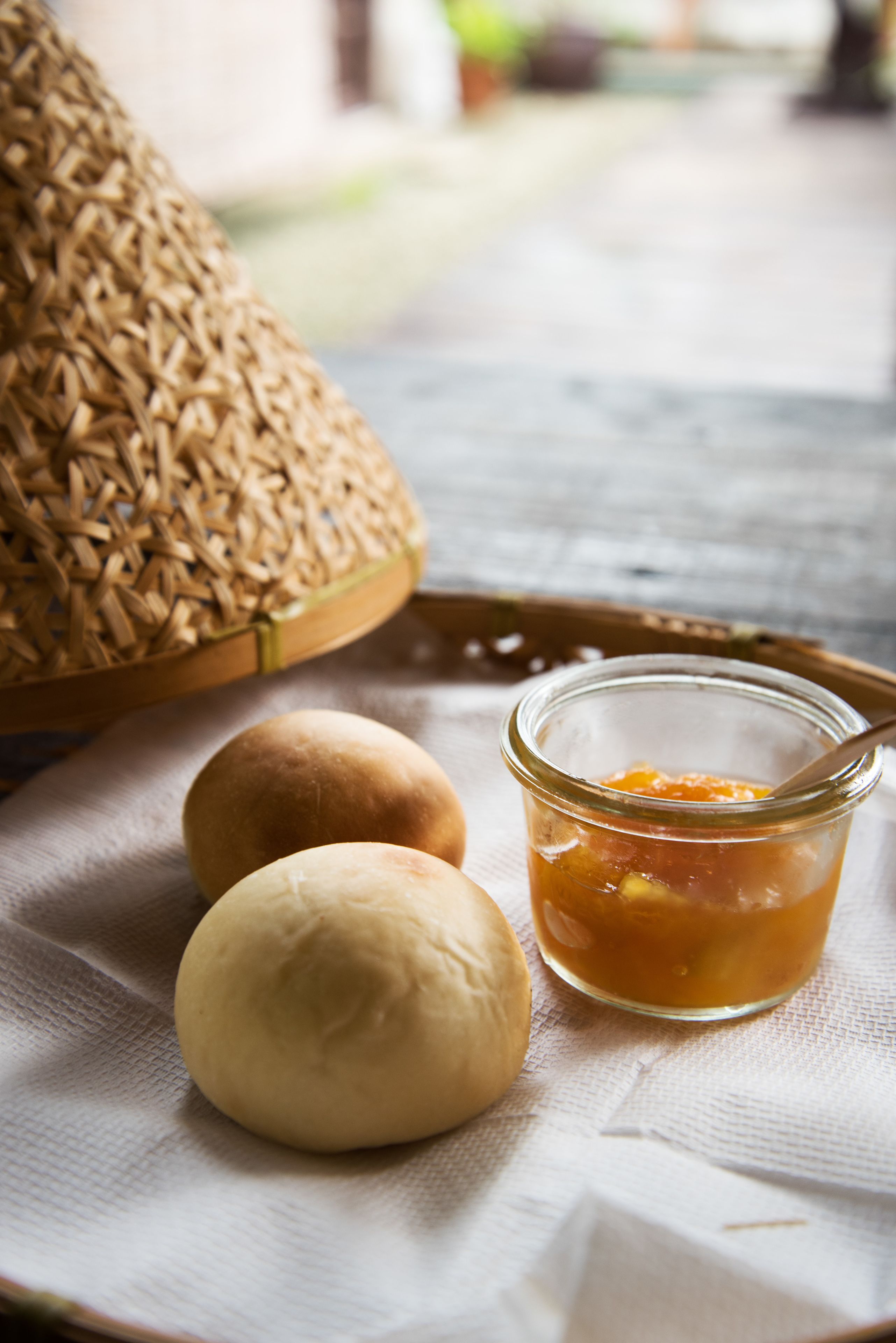 Eine Schale mit zwei Brötchen und einem Marmeladenglas auf einem Tuch.