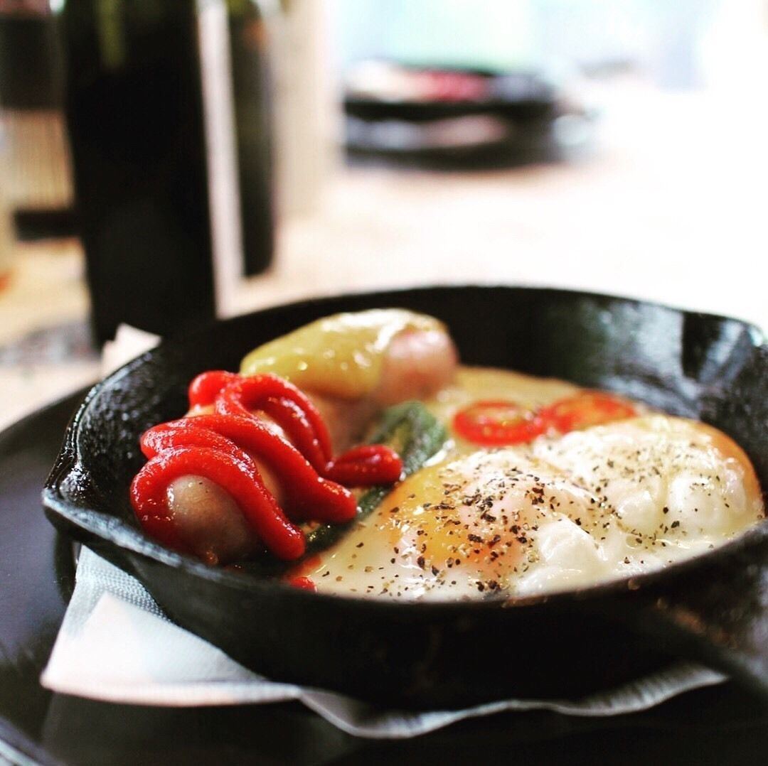 A skillet with a poached egg, red peppers, and green vegetables.