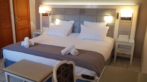 A neatly made bed with white linens, a bedside table with a lamp, and a wooden wardrobe.