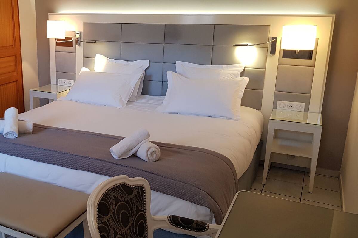 Un lit bien fait, avec du linge de lit blanc, une table de chevet avec une lampe et une armoire en bois.