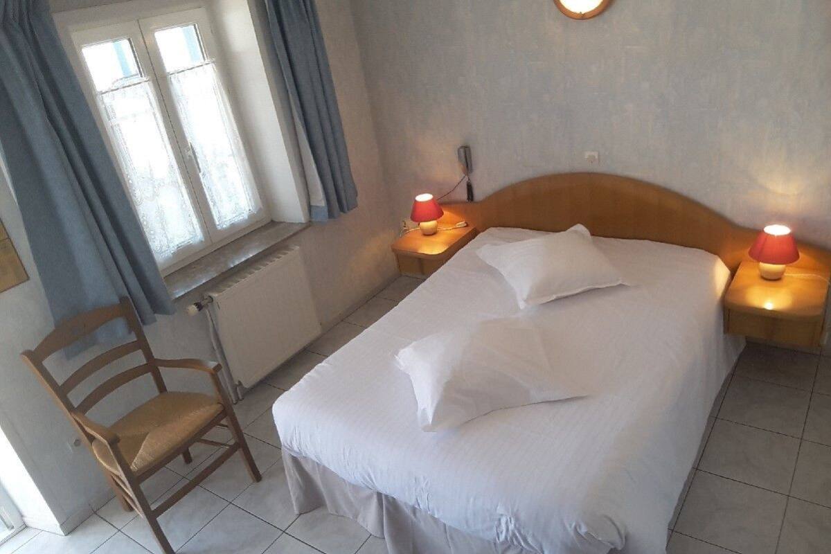 Une chambre à coucher comprenant un lit, deux lampes de chevet, une chaise, une fenêtre avec des rideaux et un radiateur.