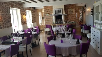 Um restaurante com paredes de pedra, cadeiras roxas e mesas brancas.