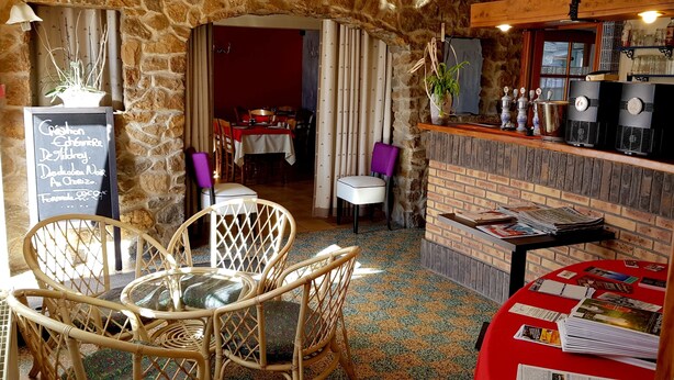 A cozy restaurant with a stone archway, wicker chairs, a red table with magazines, and a brick bar area with vintage-style refrigerators.