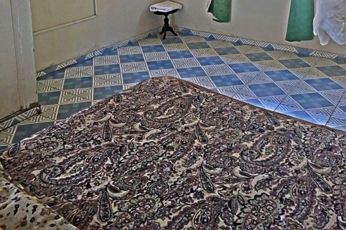 Een kamer met een kamerbreed tapijt, een bed, een klein tafeltje, een raam met gordijnen en een luchtbeheersingsunit aan de muur.