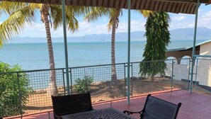 Een overdekt terras met een tafel en vier banken, met uitzicht op een strand en de oceaan.
