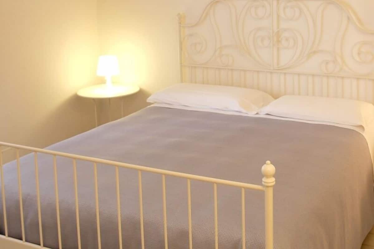 Una cama con estructura metálica y cabecera decorada con ornamentos de volutas.