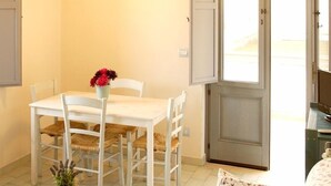 A dining area with a white table and chairs, a vase with red flowers, and a door leading outside. - B&B Midiè (Fasano)