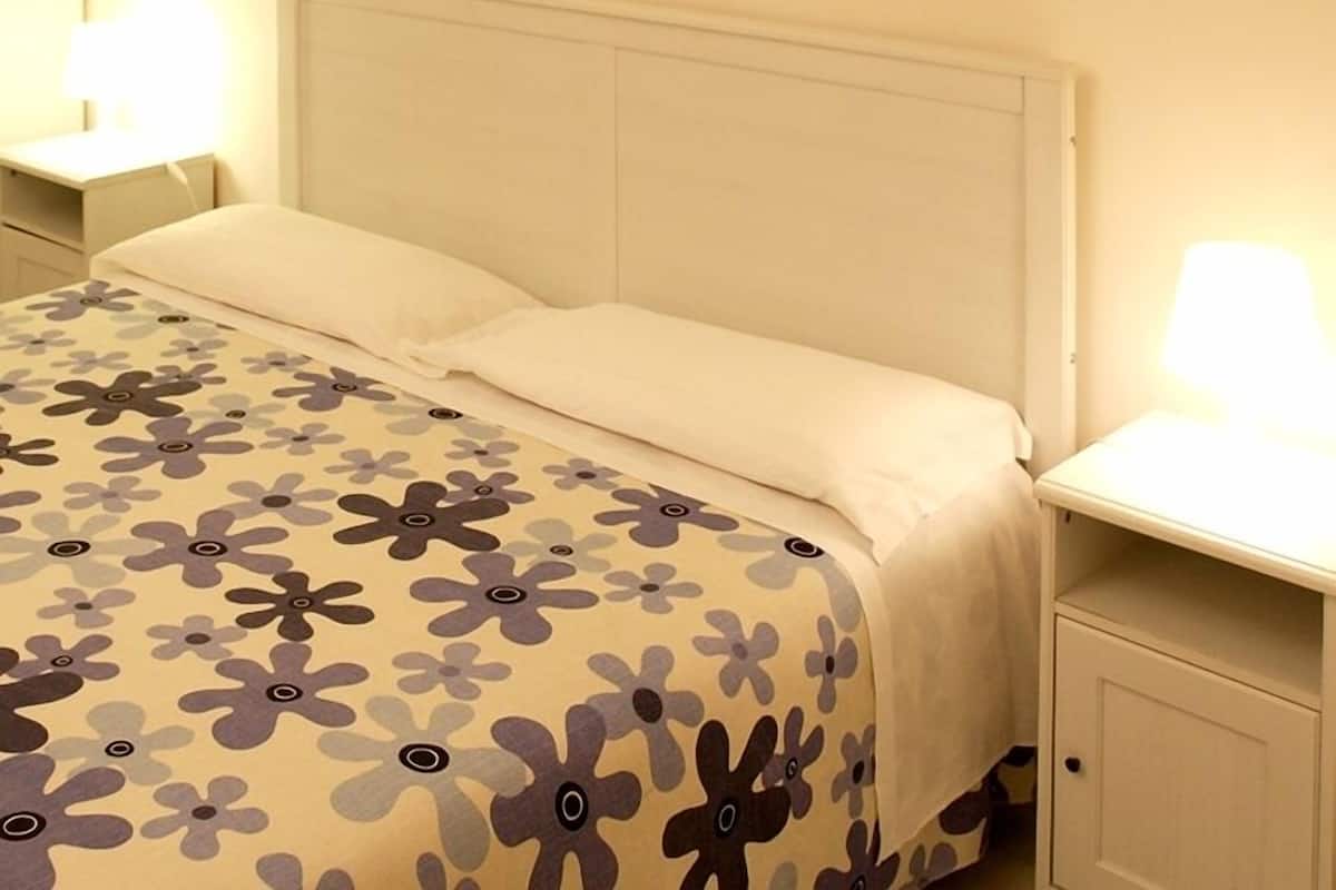 Una cama con una colcha estampada con flores, dos lámparas de noche y una mesita de noche con un cajón.