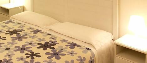 A bed with a floral bedspread, two bedside lamps, and a nightstand with a drawer.