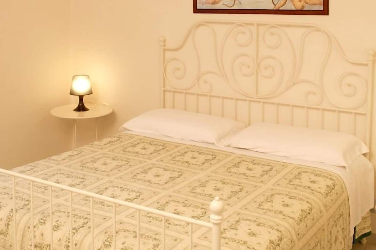Una cama bien hecha con un edredón estampado, un cabecero blanco y una lámpara de noche.