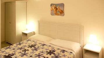 Um quarto com uma cama, duas mesas de cabeceira, um criado-mudo e um guarda-roupa, além de um quadro na parede.