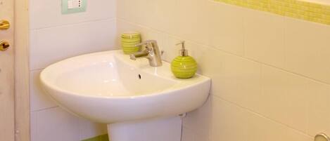 A bathroom with a white sink, green and yellow tiled walls, a green soap dispenser, and a light switch on the wall.