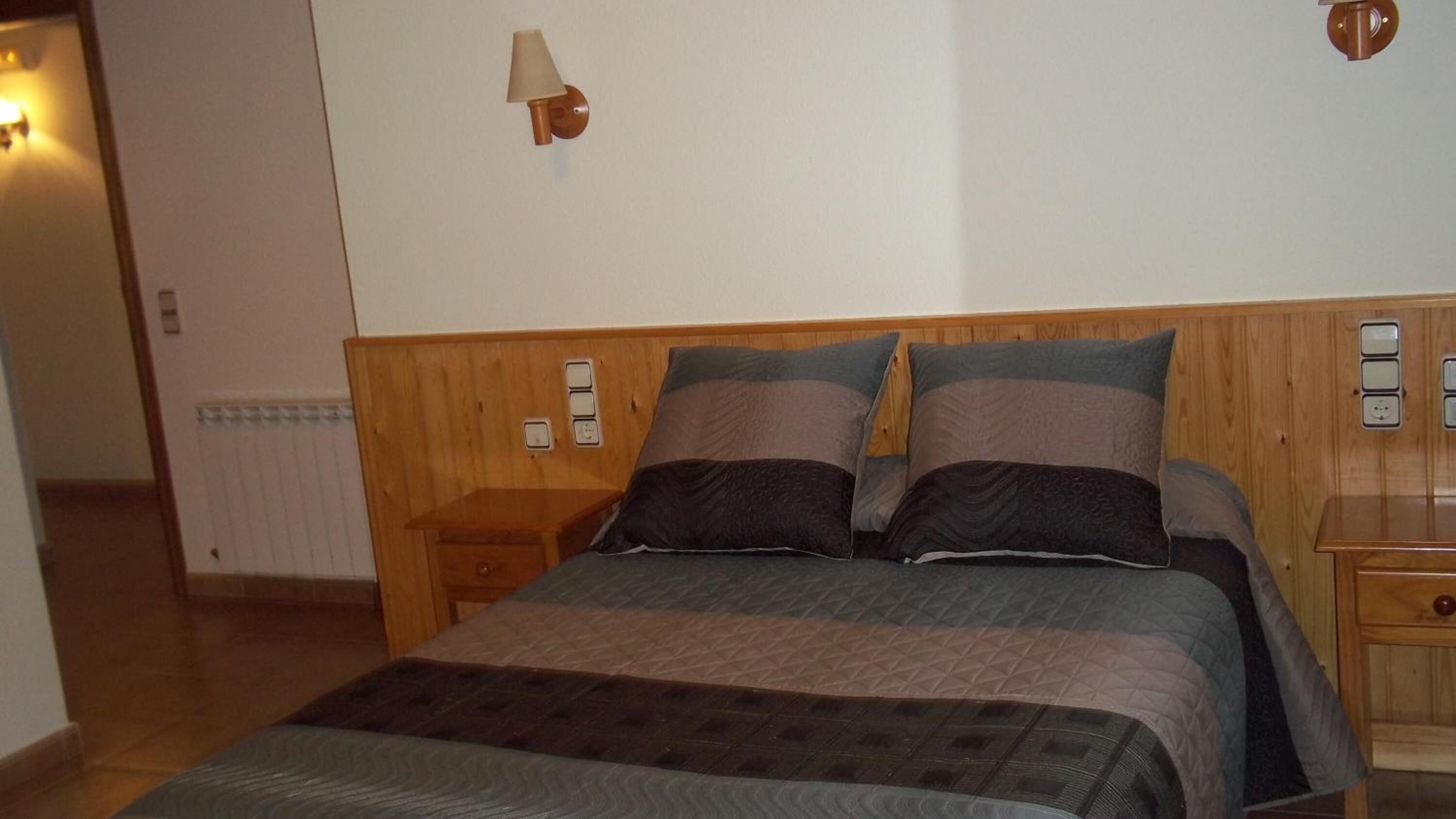 Une chambre à coucher avec une tête de lit en bois, un lit avec plusieurs oreillers, une table de chevet et une lampe fixée au mur.
