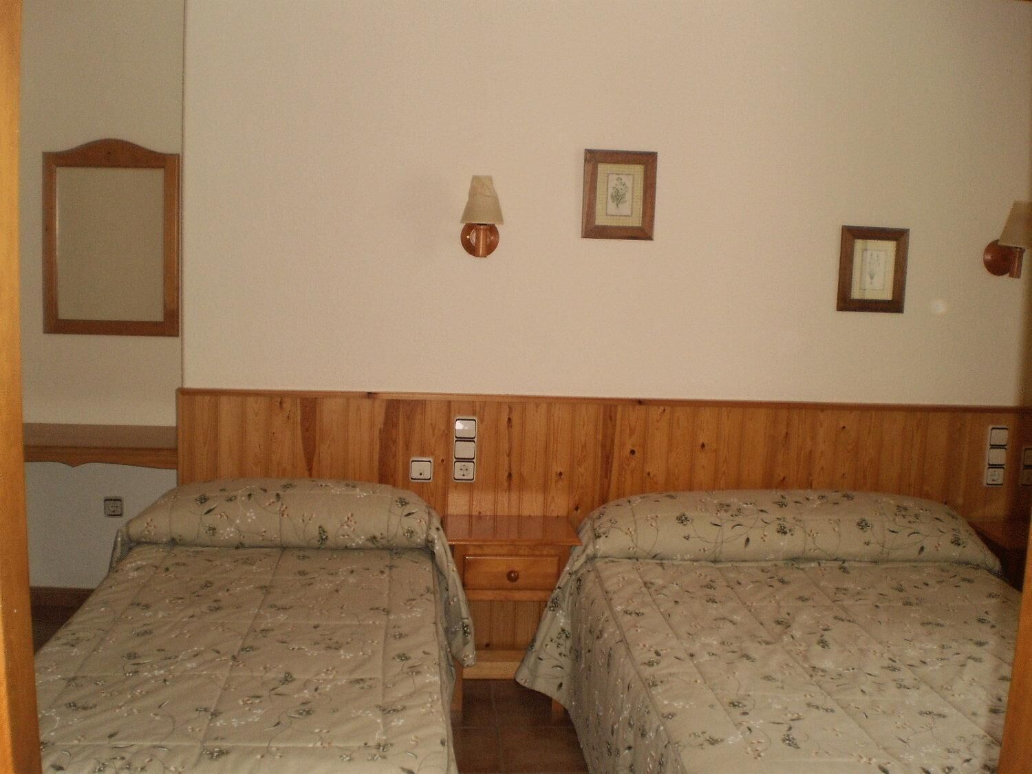 Een kamer met twee bedden, een houten hoofdbord, wandlampen en ingelijste foto's.