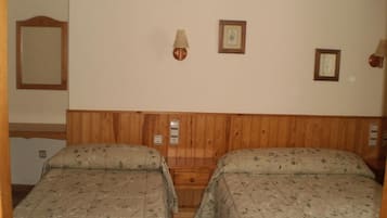 Een kamer met twee bedden, een houten hoofdbord, wandlampen en ingelijste foto's.