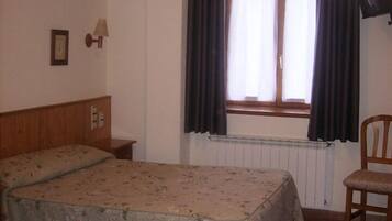 Een kamer met twee bedden, een stoel, een raam met gordijnen, een wandlamp en een radiator.
