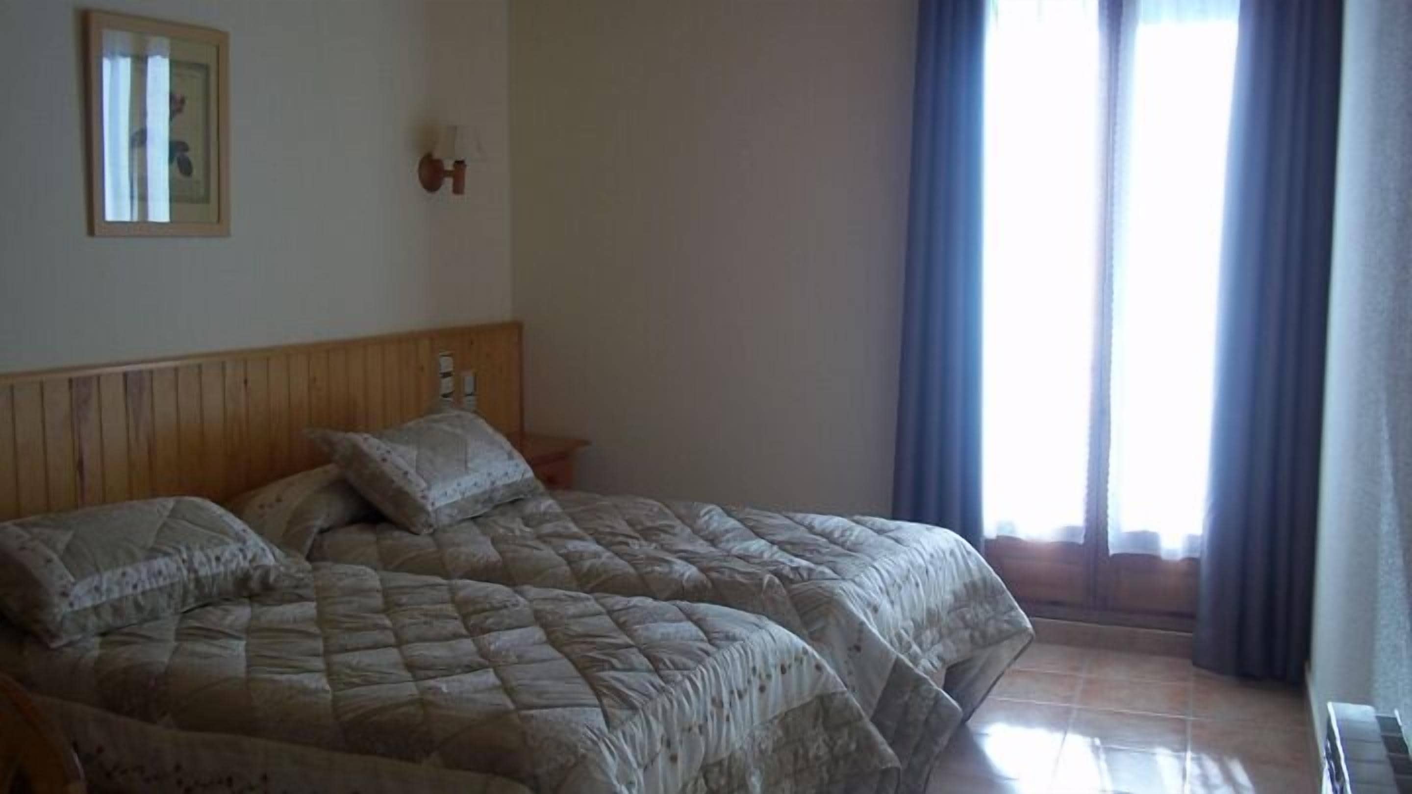 A double bed with a wooden headboard, a bedside table with a lamp, and a window with curtains.