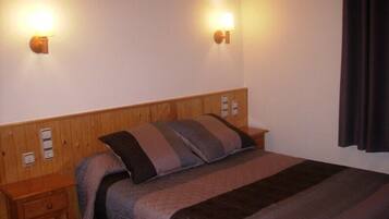 Quarto de hotel com cabeceira de madeira, cama com cobertura acolchoada, duas mesinhas de cabeceira e luminárias fixadas na parede.
