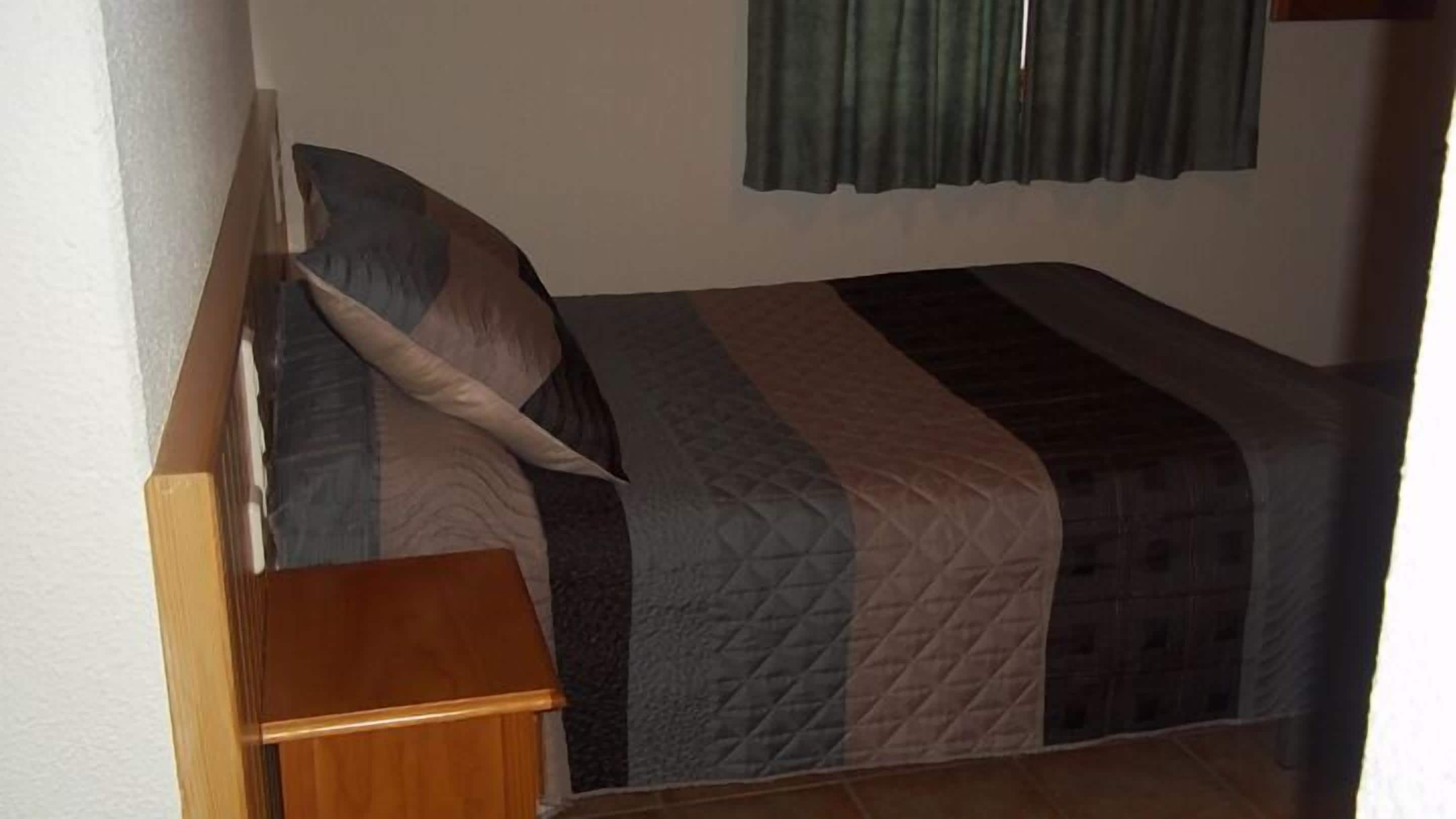 Uma cama de solteiro com cabeceira de madeira, mesa de cabeceira e colcha acolchoada.