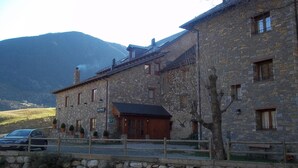 Un bâtiment en pierre avec une porte et des fenêtres en bois, un espace de stationnement et une montagne en arrière-plan.