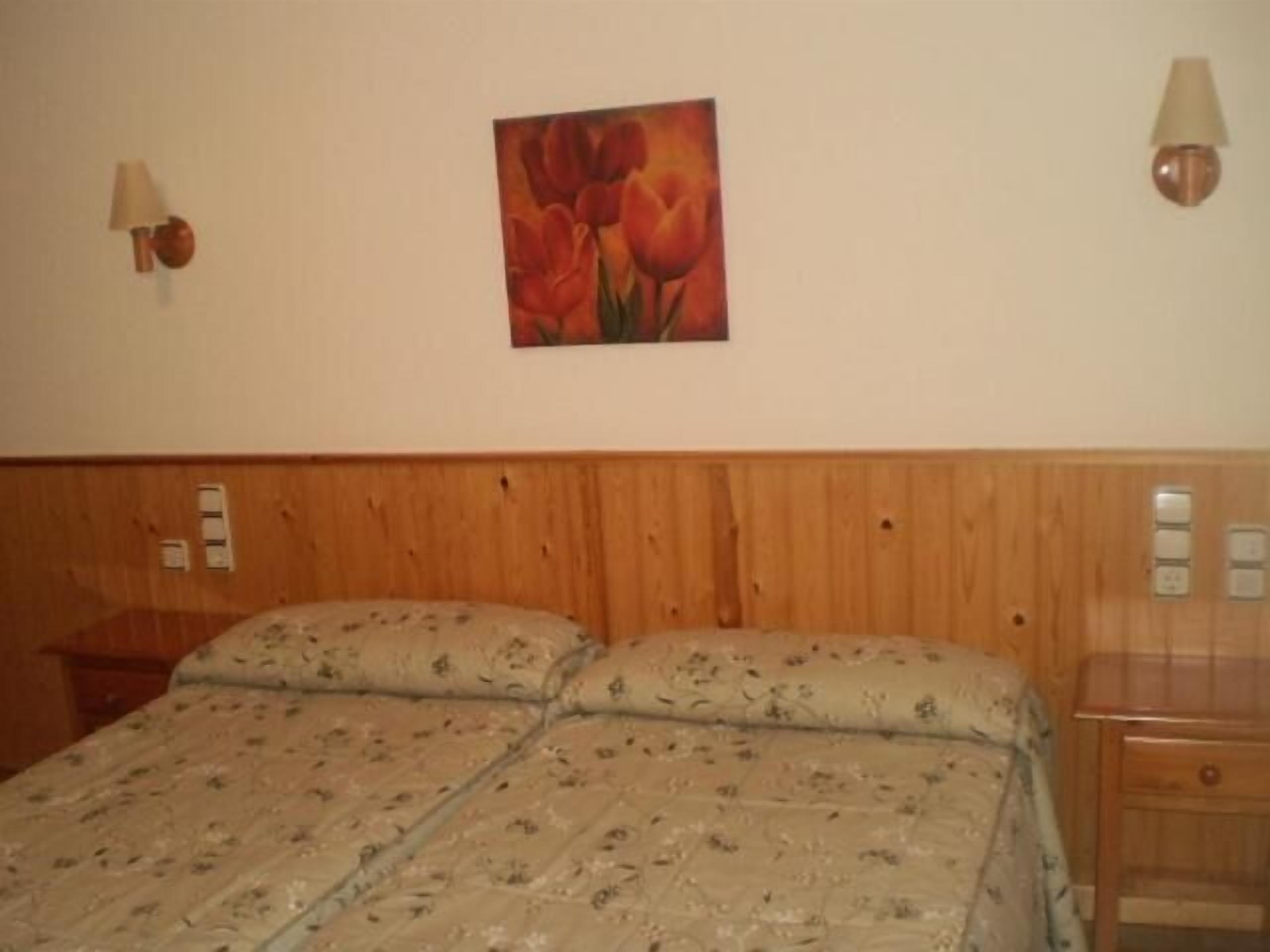 Habitación de hotel con cabecera de madera, colcha estampada con motivos florales, dos lámparas de noche y un cuadro de tulipanes en la pared.