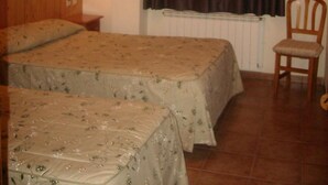 Une chambre avec deux lits, une chaise, un téléviseur fixé au mur et une fenêtre avec des rideaux.