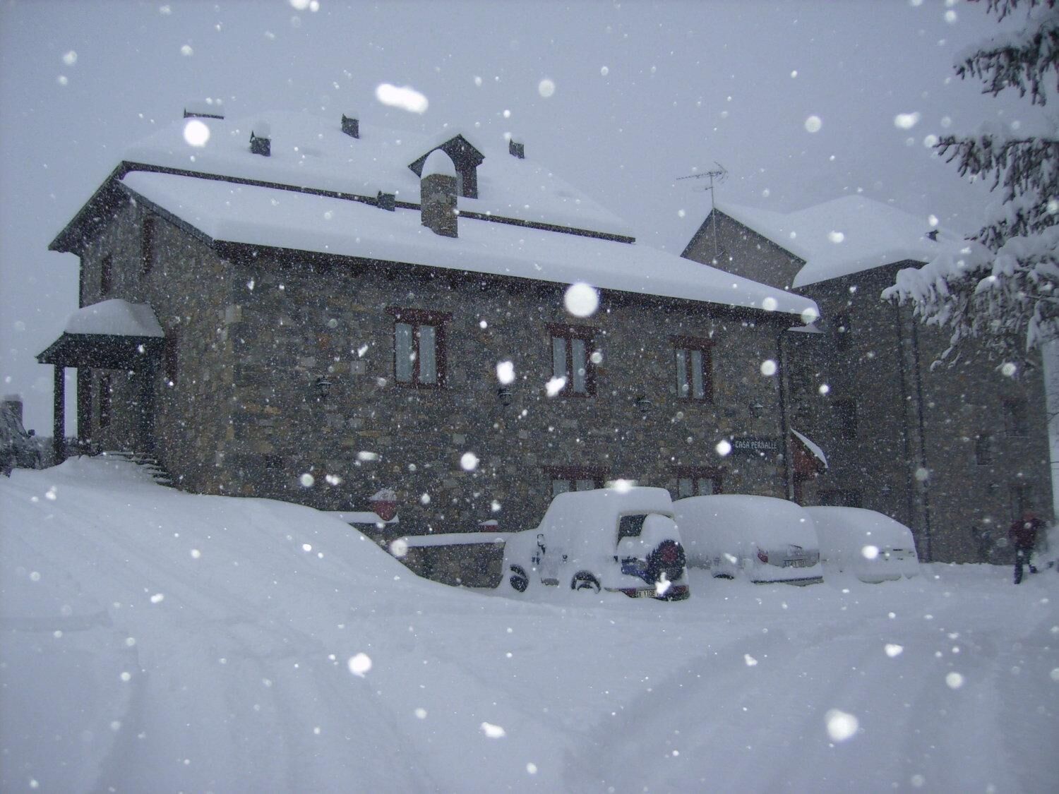 A stone building with a snow-covered roof and multiple windows, surrounded by snow.