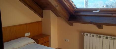 A bedroom with a sloped ceiling, a bed with a floral bedspread, a nightstand, a radiator, and a view of a tower through a skylight.