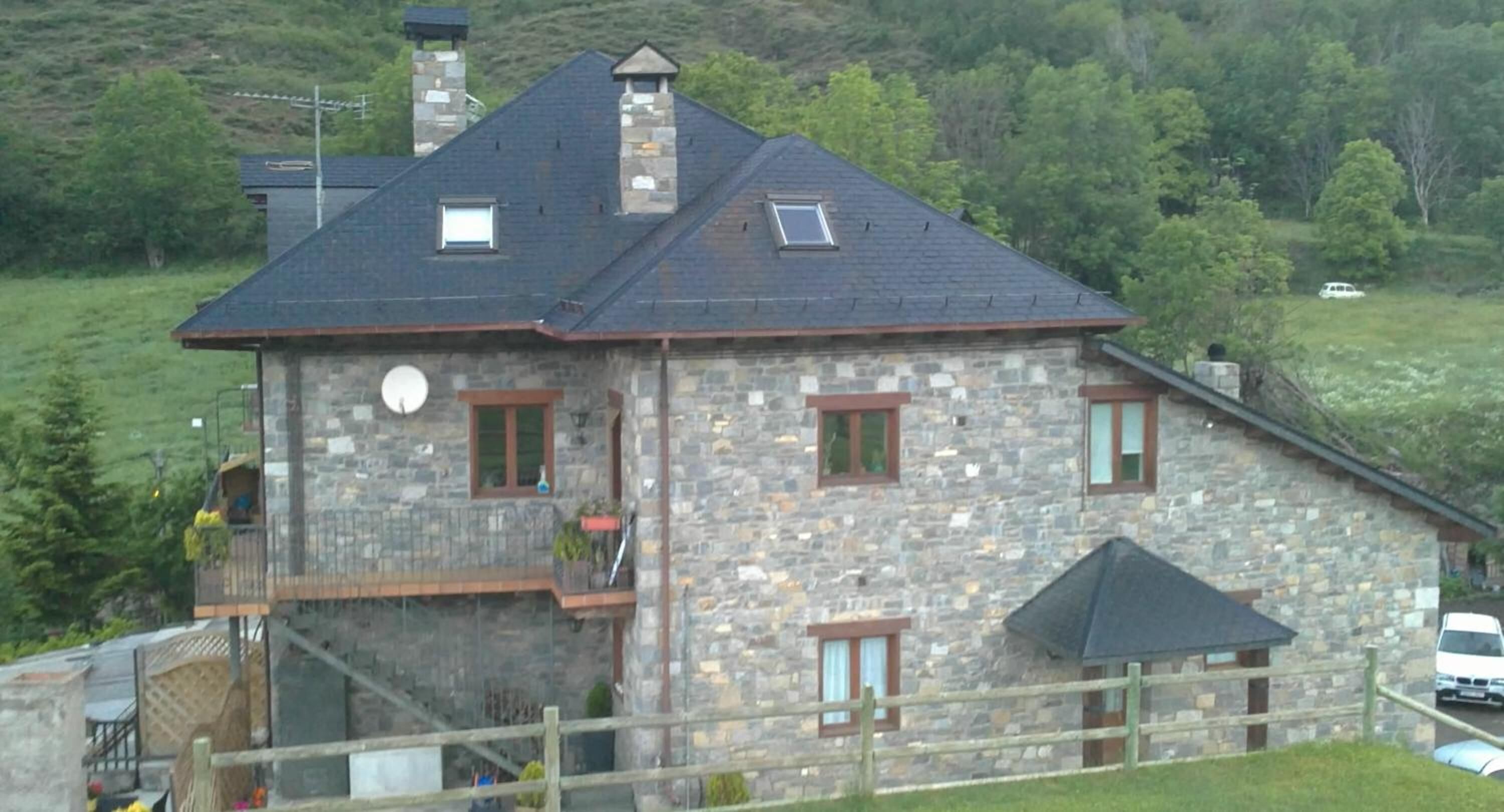 Una casa de piedra con techo inclinado, un balcón y una estructura adosada más pequeña con techo.