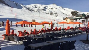 Sitzgelegenheiten im Freien mit Tischen und Stühlen, ein Skilift im Hintergrund und ein schneebedeckter Berg.