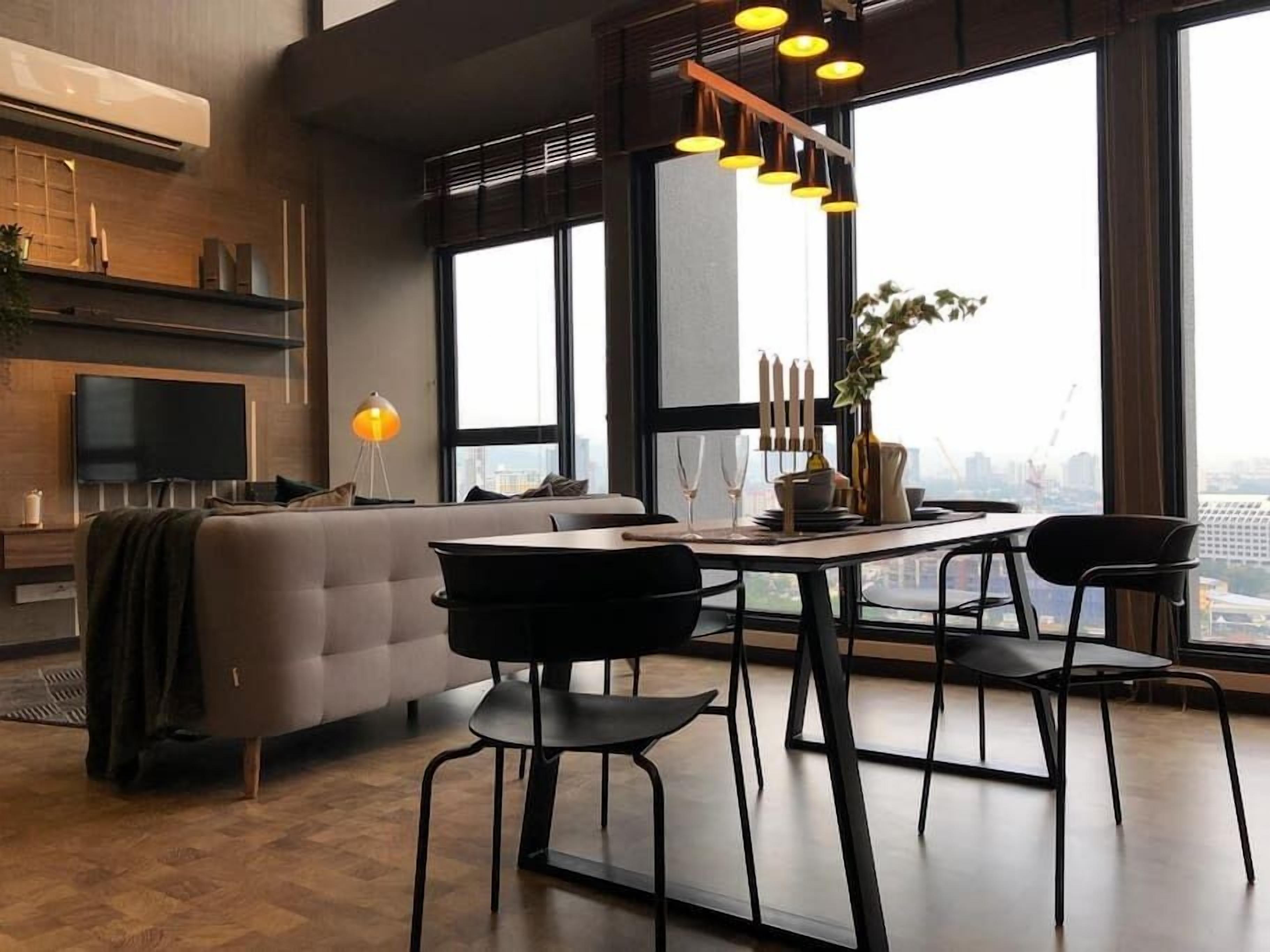 Un salon moderne avec un canapé, une table à manger et des chaises. On y trouve également un téléviseur, un lampadaire et une grande fenêtre donnant sur la ville.