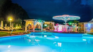 Une piscine agrémentée d’une fontaine et d’un carrousel, entourée de chaises longues et d’un espace de repos abrité.