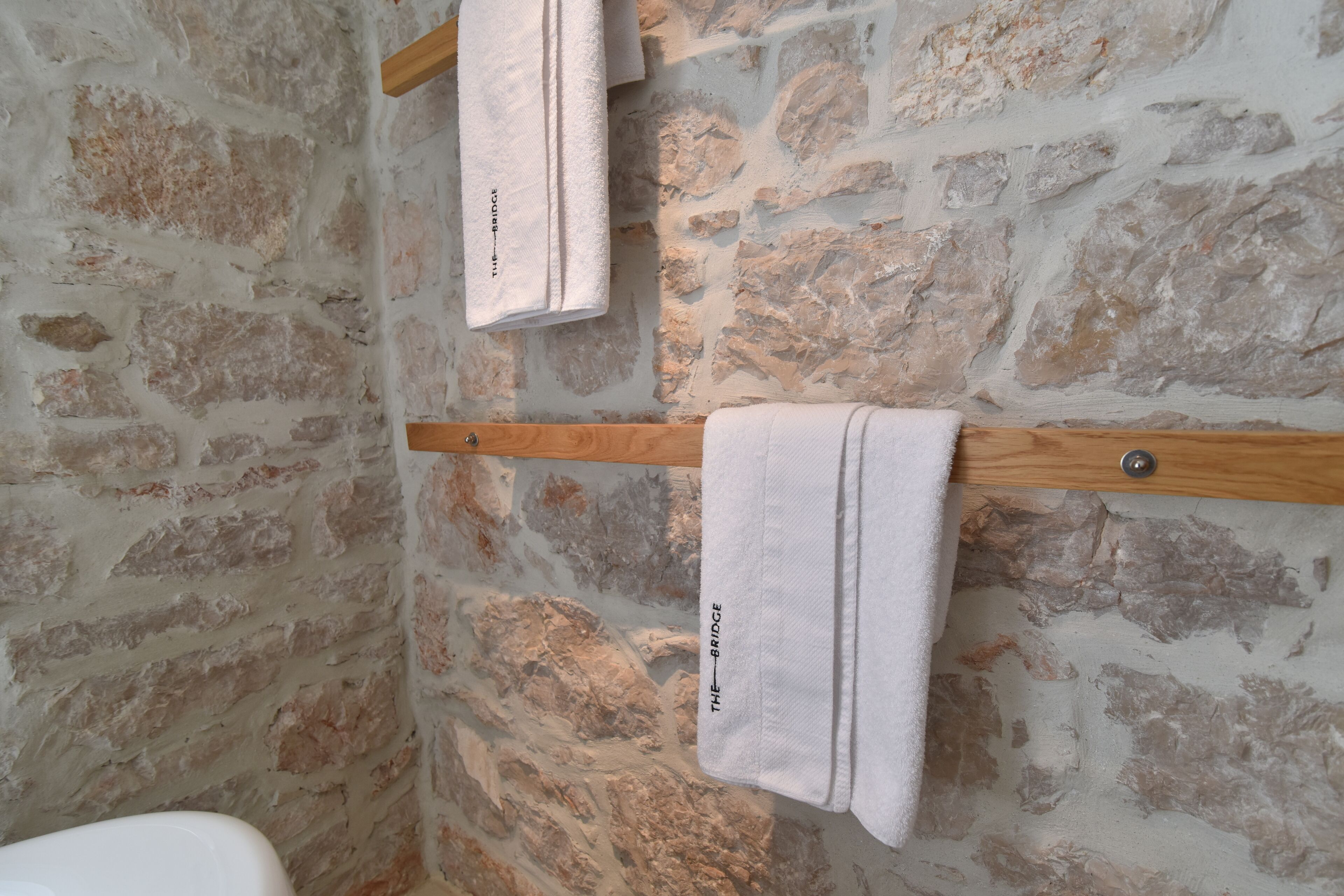 A bathroom with a stone wall and wooden towel racks.