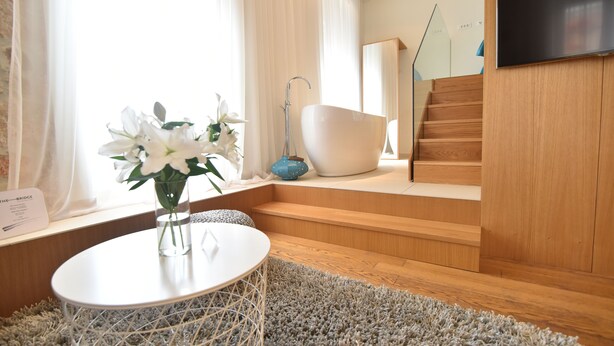 A modern bathroom with a bathtub, wooden stairs, and a flat-screen TV mounted on the wall. - The Bridge Luxury Apartments (Zadar)