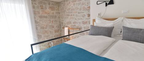 A bedroom with a stone wall, a bed with white and blue bedding, and a nightstand with a lamp.