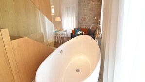 A modern bathroom with a freestanding bathtub, a wooden vanity, and a stone accent wall. - The Bridge Luxury Apartments (Zadar)
