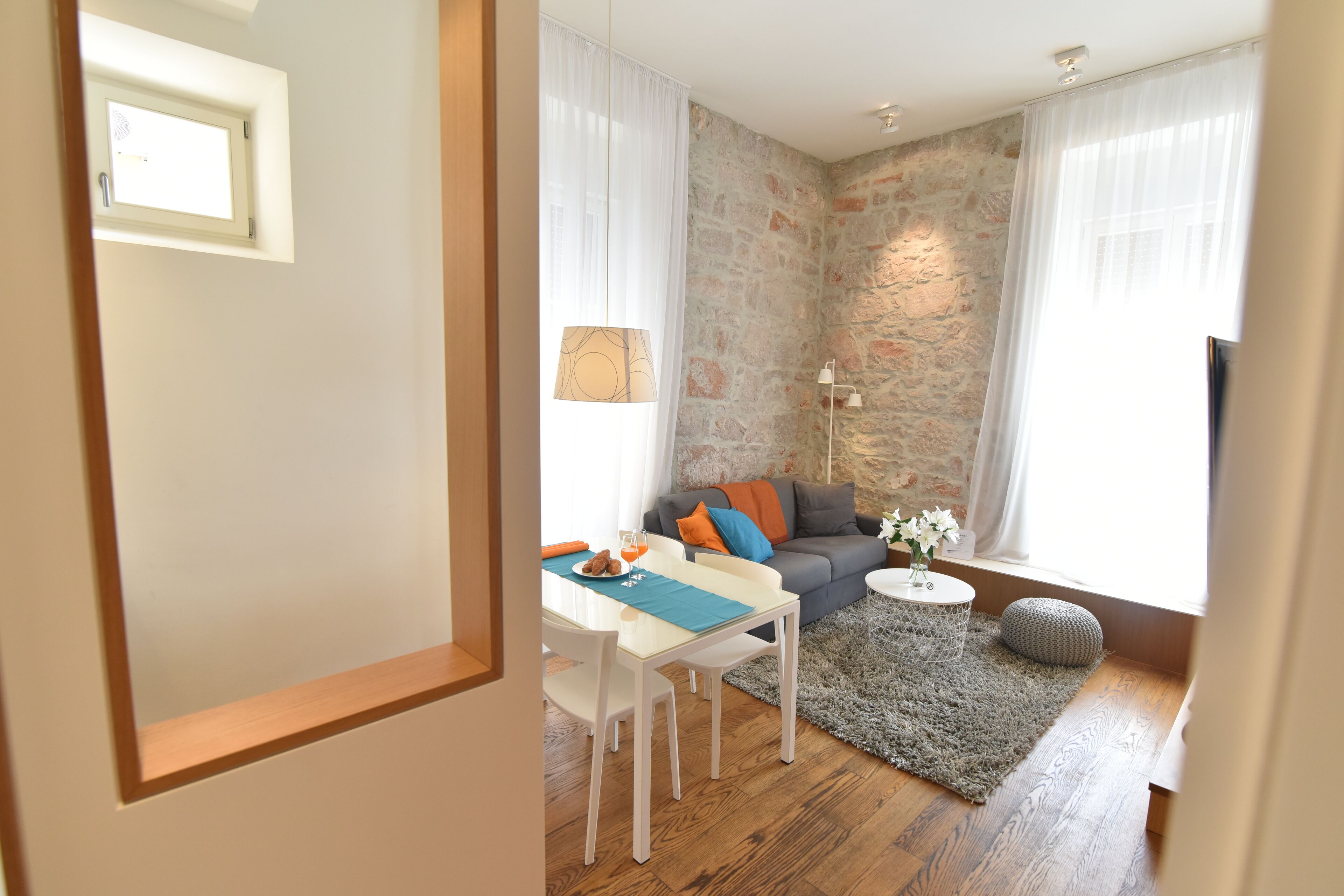 A modern living room with a stone accent wall, a dining area with a table and chairs, and a cozy seating area with a sofa and cushions.