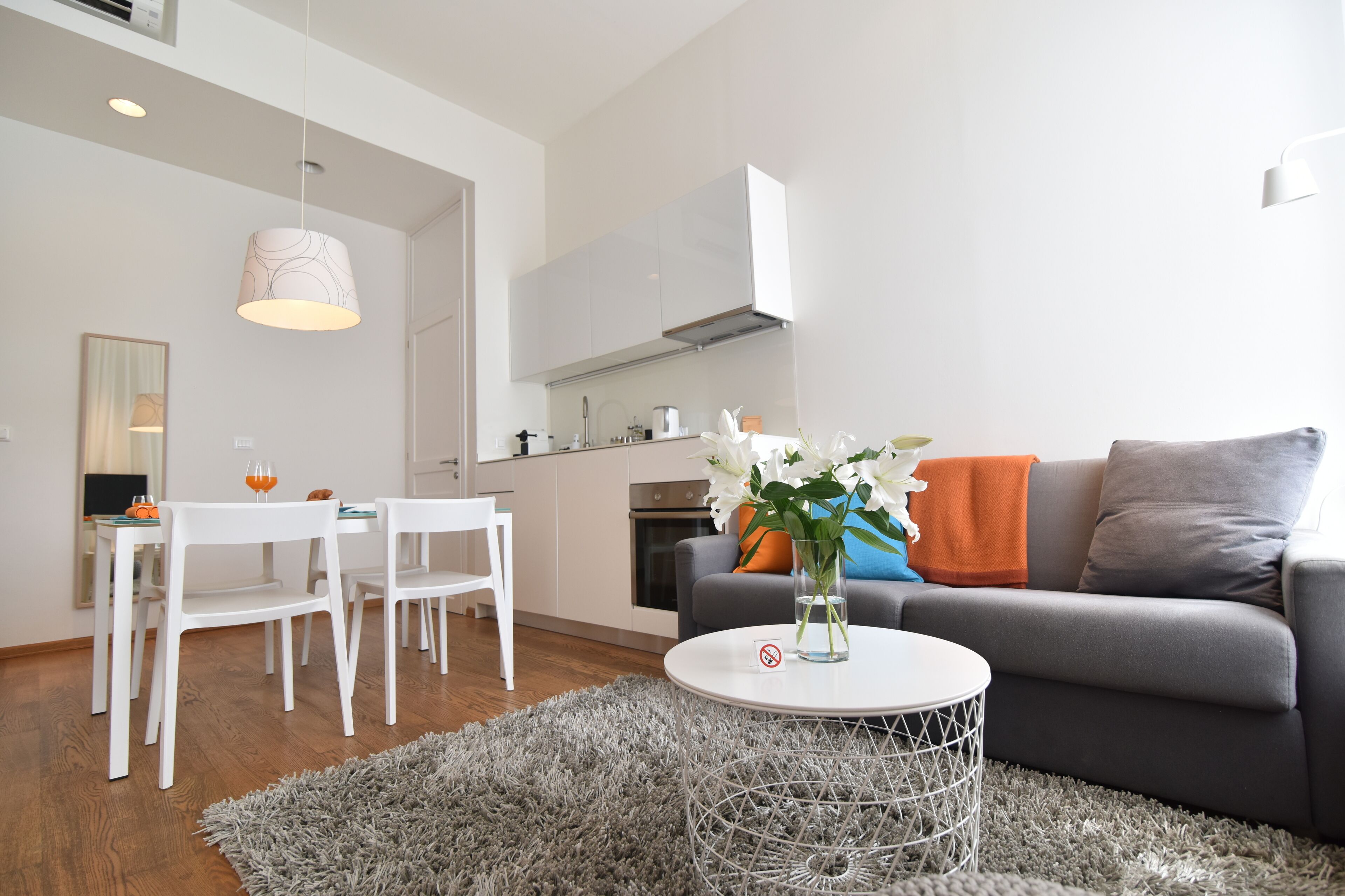 A modern living room with a grey sofa, white chairs, a round coffee table, and a dining area with a white table and chairs.
