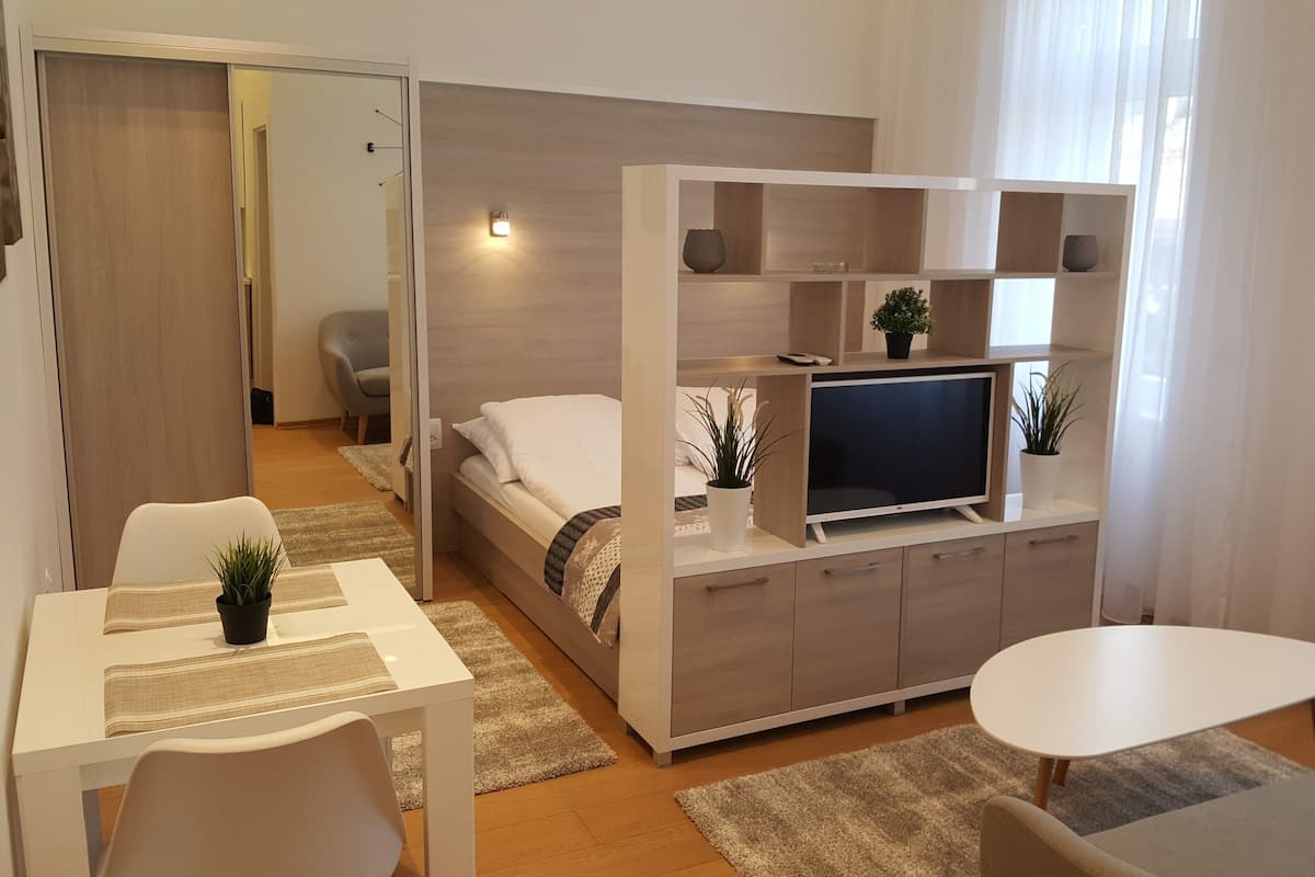 Ein kleines Hotelzimmer mit Bett, Fernseher, Schreibtisch und Stuhl.