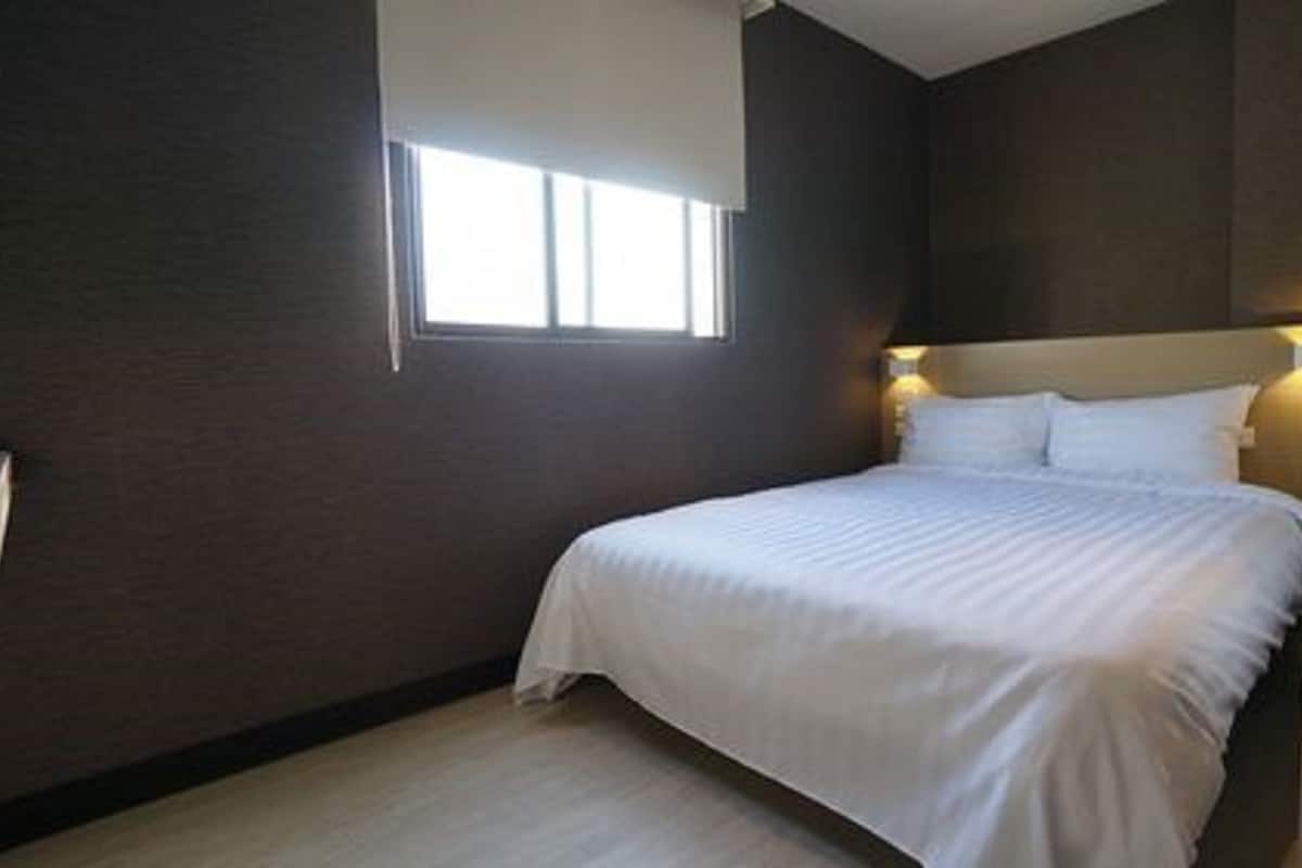 Une chambre avec un grand lit, une fenêtre et un luminaire fixé au mur.