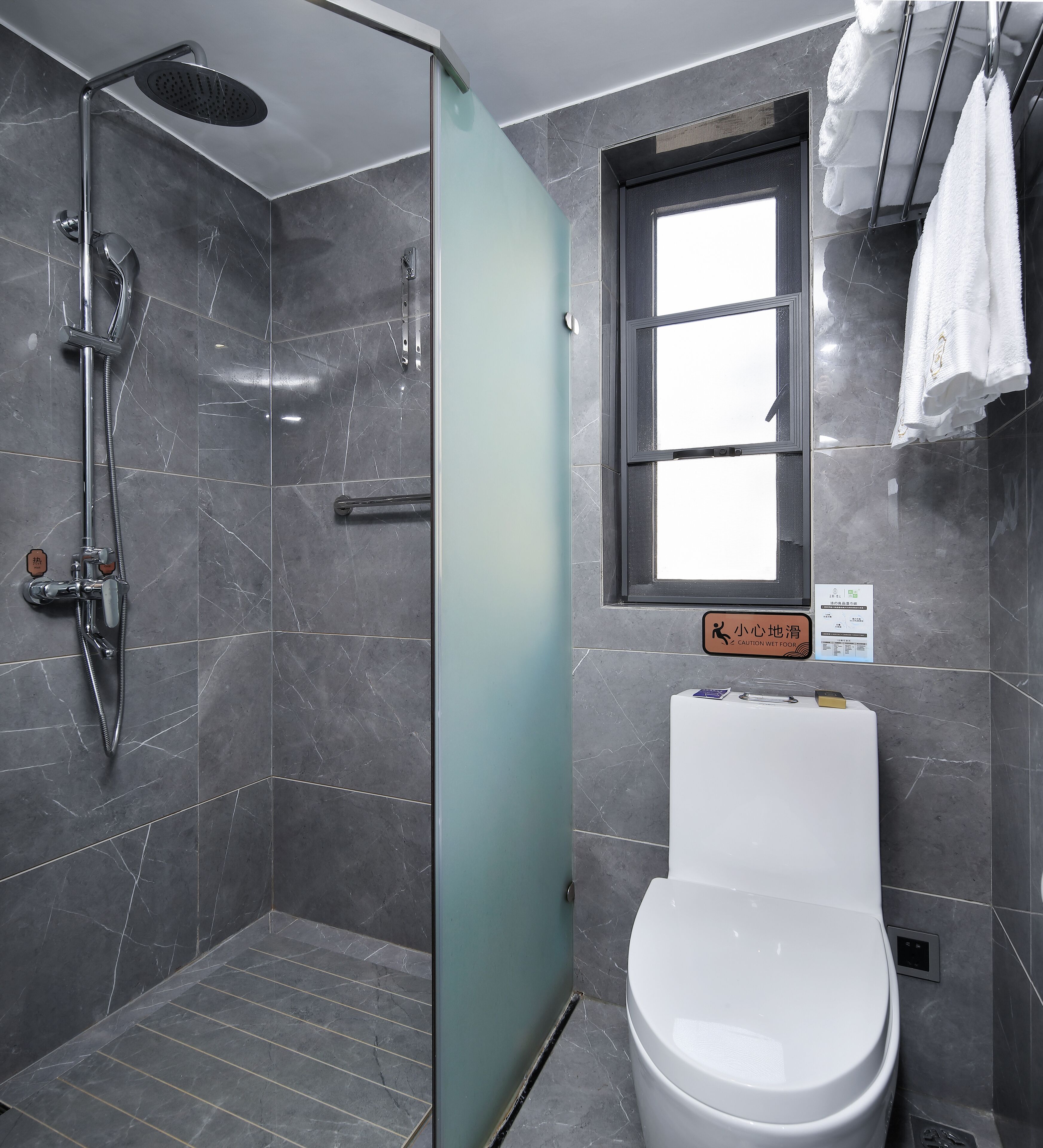 A modern bathroom with a glass shower enclosure, a toilet, and a window.