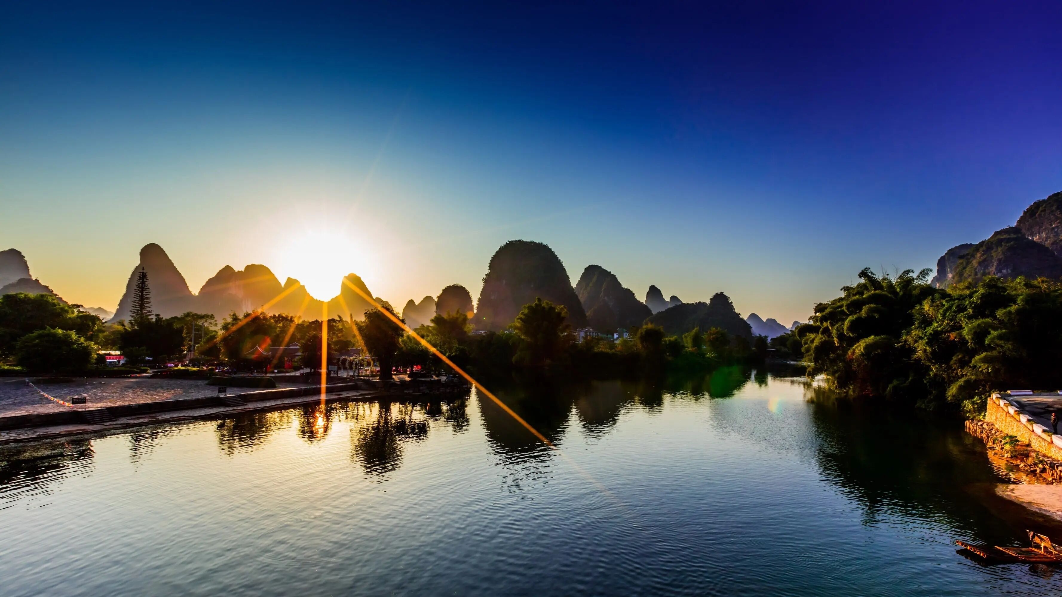 A serene riverside view with mountains in the background and a clear sky.