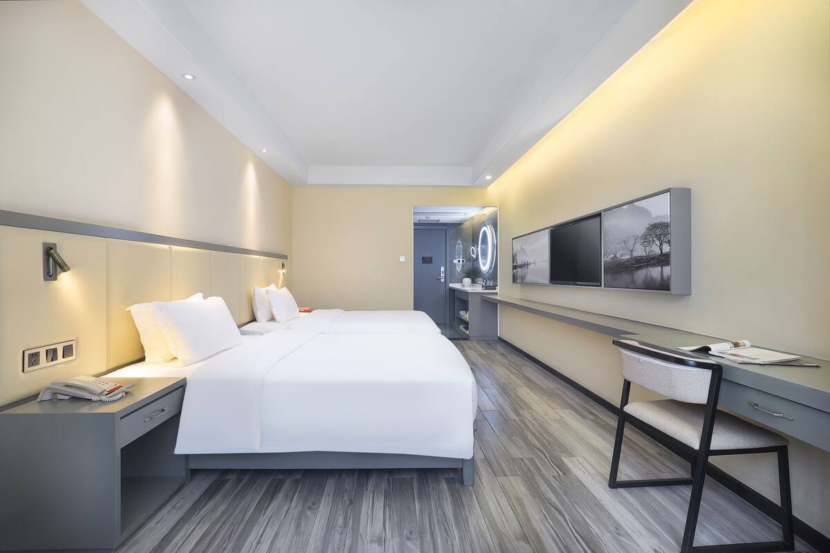 Moderni hotellihuone, jossa on suuri sänky, yöpöydät, työpöytä, tuoli, peili ja televisio.