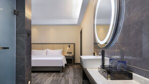 Una habitación de hotel moderna con una cama grande, un baño con tocador y un tragaluz sobre la cama.