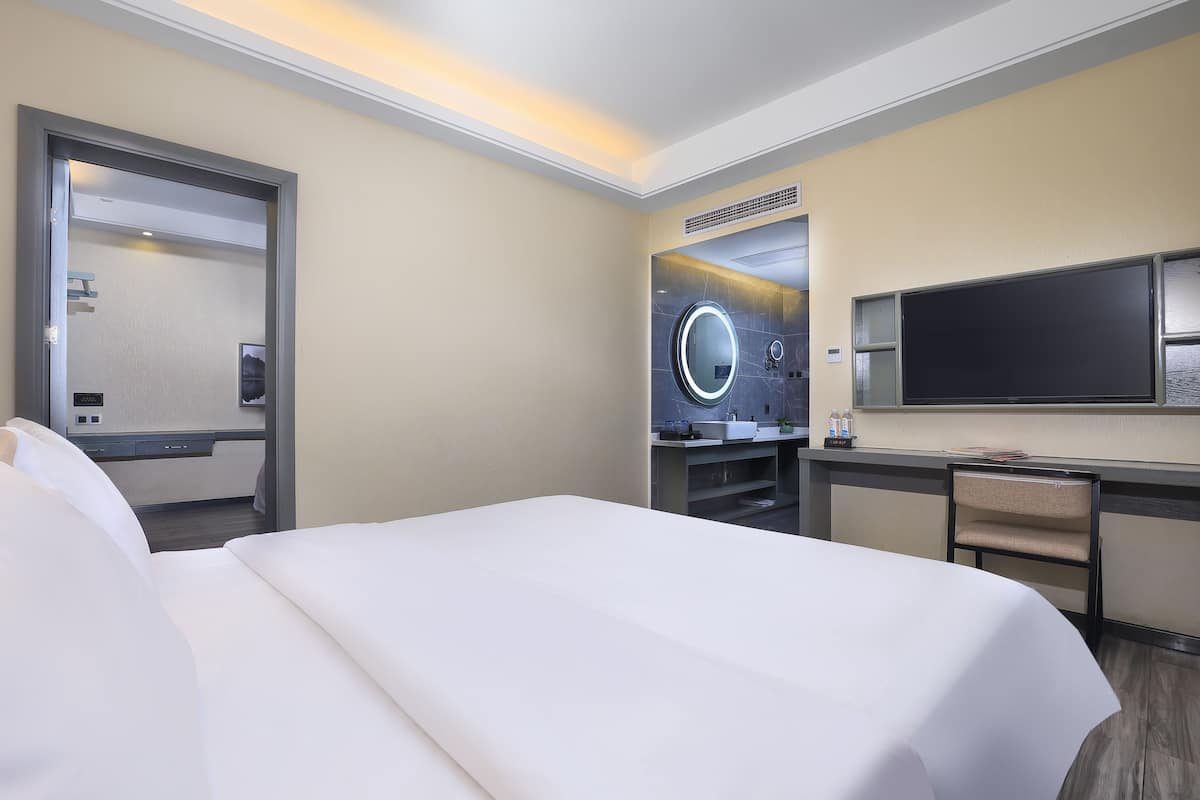 Hotellihuone, jossa on suuri sänky, työpöytä tuolilla, televisio ja peili.