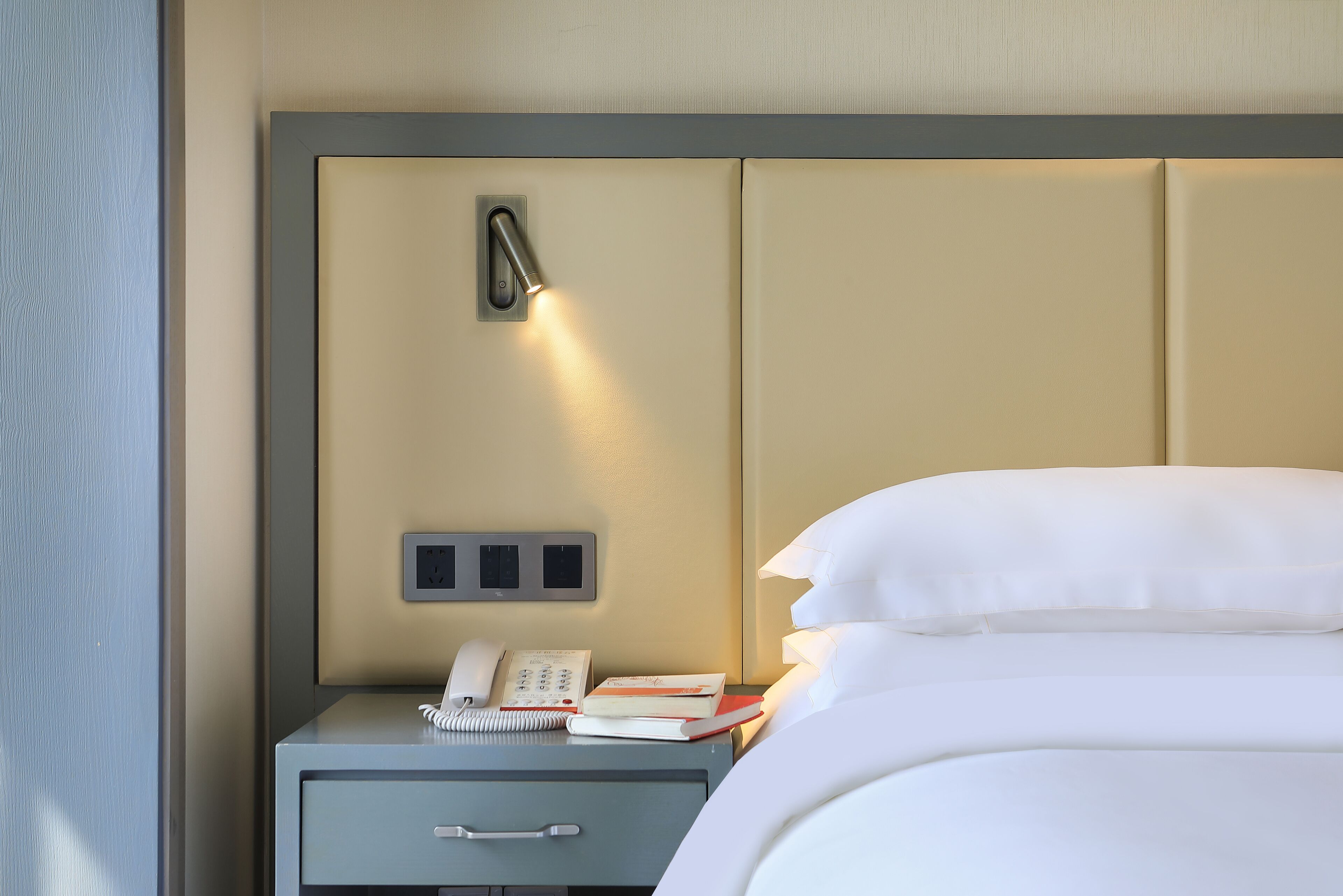Een verzorgde hotelkamer met een bed, nachtkastje met lamp, telefoon en notitieboekje.