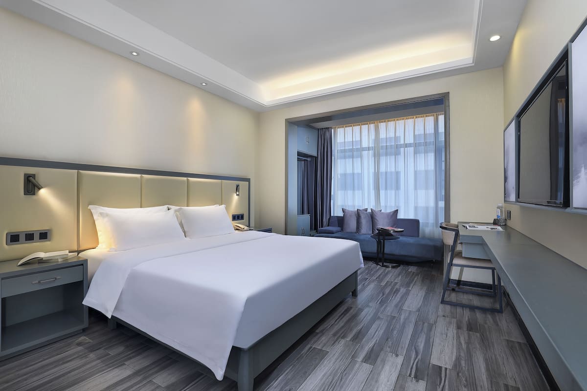 Moderni hotellihuone, jossa on suuri sänky, työpöytä ja oleskelualue.