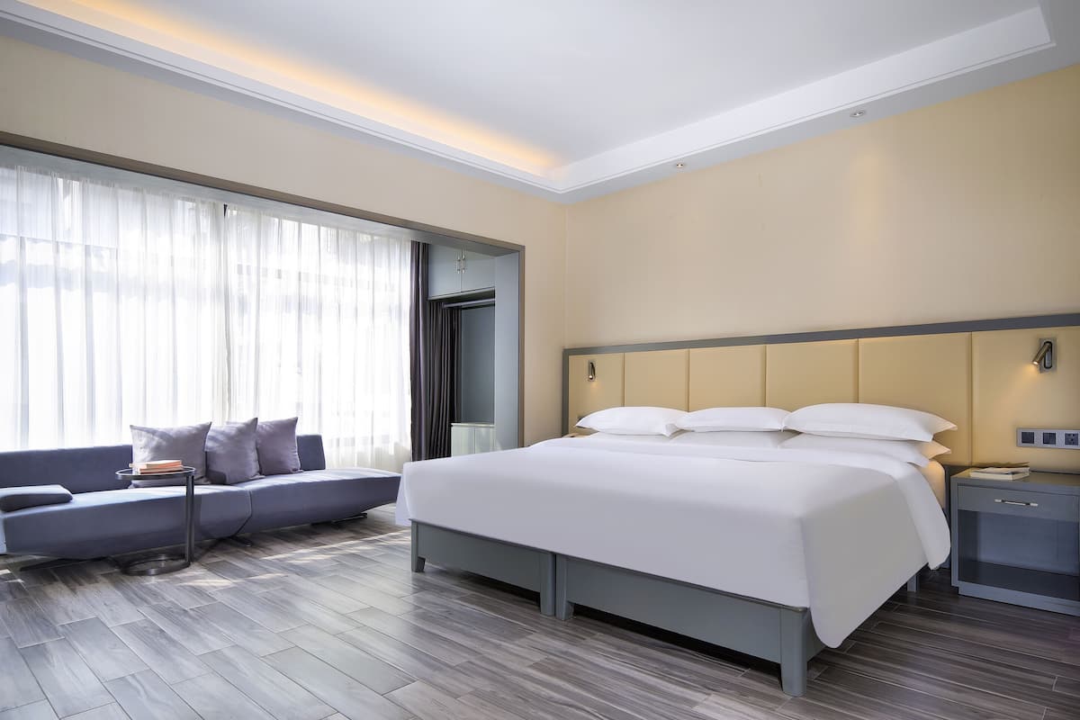 Moderni hotellihuone, jossa on suuri sänky, sohva, yöpöytä ja ikkuna, jossa on verhot.